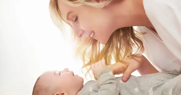 Uśmiechnięta mama pochyla się nad dzieckiem, które ma czkawkę u noworodka.