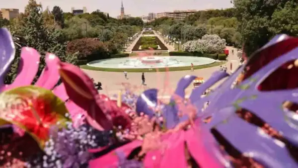 Flores vibrantes en primer plano, con el parque grande Zaragoza florece al fondo, destacando una fuente y senderos verdes.
