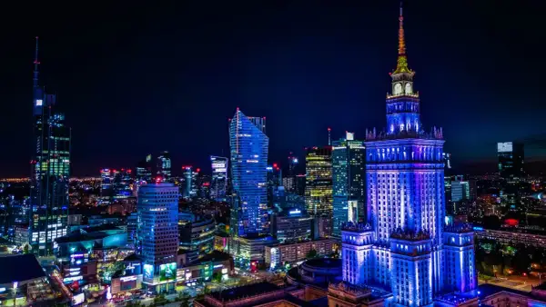 Nocna panorama Warszawy z Pałacem Kultury oświetlonym na niebiesko. Miasto tętni życiem, a liczne światła zapowiadają ciekawe warszawa wydarzenia.