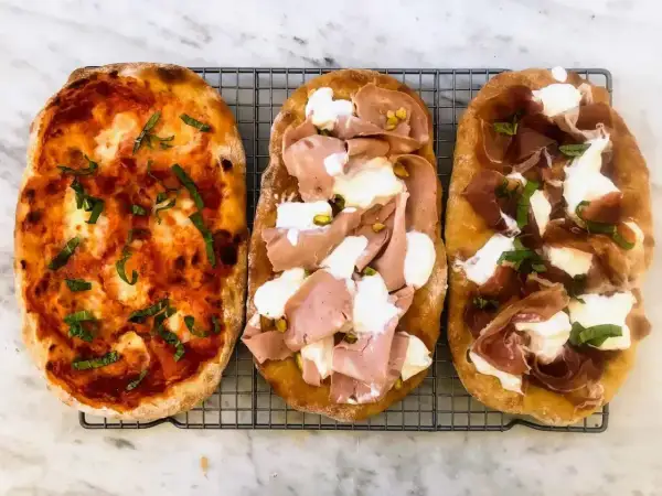 Trzy pyszne pinsy: jedna z sosem pomidorowym i bazylią, druga z mortadelą i pistacjami, trzecia z szynką parmeńską i mozzarellą. Tak wygląda pinsa co to!