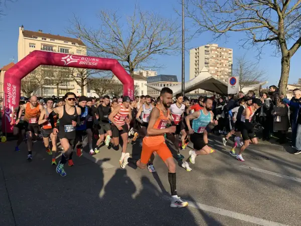 Départ d'une course à Bourg-en-Bresse sous un ciel bleu. Des coureurs s'élancent sous une arche rose.