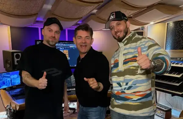 Mariusz Kalaga, jedna z gwiazd, w studiu nagraniowym z przyjaciółmi. Wszyscy pokazują kciuki w górę, gotowi do tworzenia muzyki.