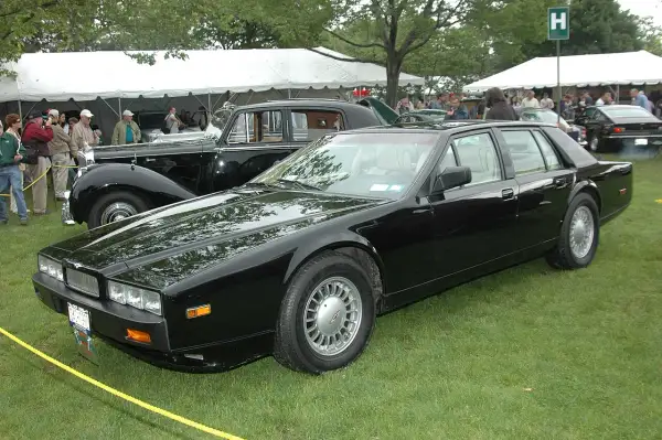 Svart Aston Martin Lagonda står på gräsmatta vid ett evenemang med tält och folk i bakgrunden.