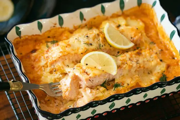 Ein köstlicher Lachs Auflauf mit geschmolzenem Käse und Zitronenscheiben, der gerade mit einer Gabel serviert wird.