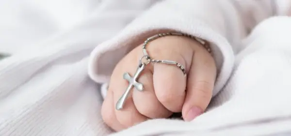 Dziecięca rączka z krzyżykiem na łańcuszku, symbol błogosławieństwa podczas chrztu dziecka.