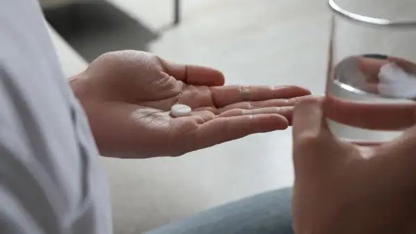 En hand håller en tablett, redo att sväljas med ett glas vatten. Detta kan vara en del av förklaringen till hur funkar antidepressiva.