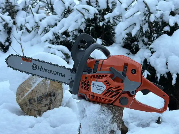 Pomarańczowa piła łańcuchowa Husqvarna 560 XP na tle zaśnieżonych drzew. Poznaj husqvarna 560 xp dane techniczne.