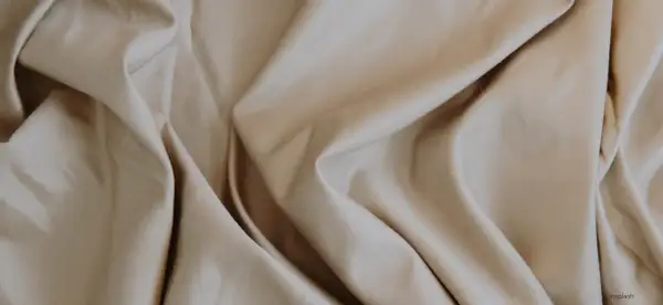 Sanfter, beige Stoff fällt in weichen Falten. Lyocell ist das, ein nachhaltiges Material, das sich so angenehm anfühlt.