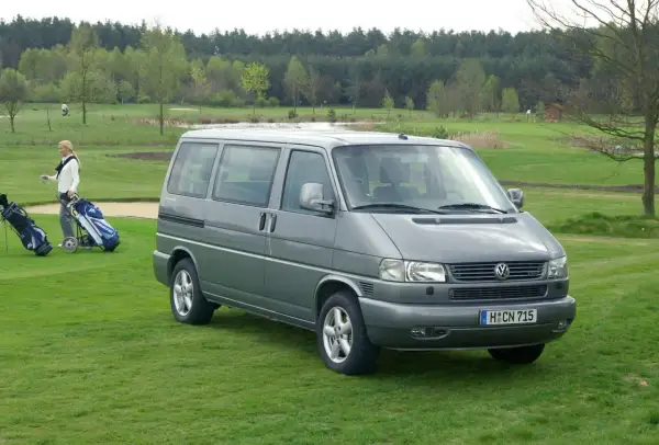 Szary VW T4 2.5 TDI 102KM na polu golfowym. Kobieta z kijami golfowymi obok.