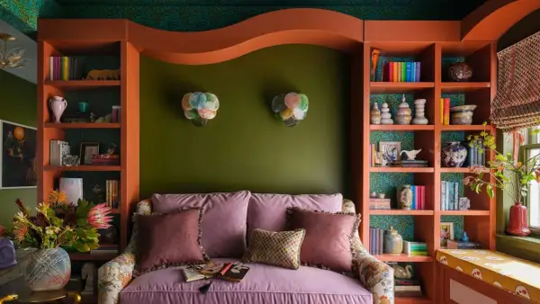 A cozy reading nook with a pink sofa, shelves filled with books and decor, and bright bold colors on the walls and shelving.