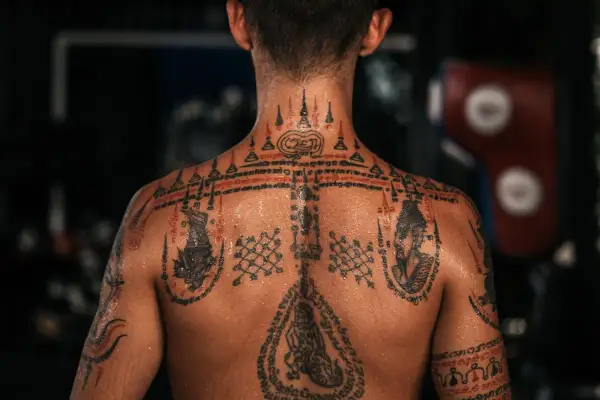 En rygg täckt av detaljerade sak yant muay thai-tatueringar, med symboler och skrifter som berättar en historia om styrka och skydd.