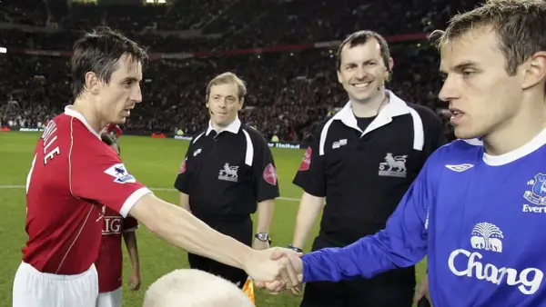 Piłkarz w czerwonej koszulce, Gary Neville, ściska dłoń rywalowi. Sędziowie obserwują.