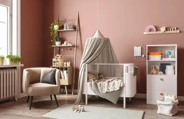 Une chambre de bébé chaleureuse avec un lit à baldaquin, une chaise confortable et des étagères pleines de jouets. Parfait pour une diy déco chambre bébé.