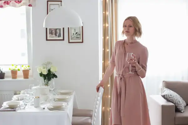 Elegancka kobieta w różowej sukience z kieliszkiem wina, przy nakrytym stole. Idealna stylizacja co na wesele.