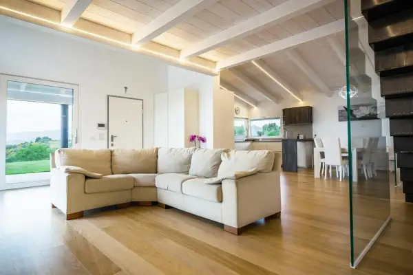 Soggiorno moderno con travi in legno di bianco, divano beige e cucina a vista.