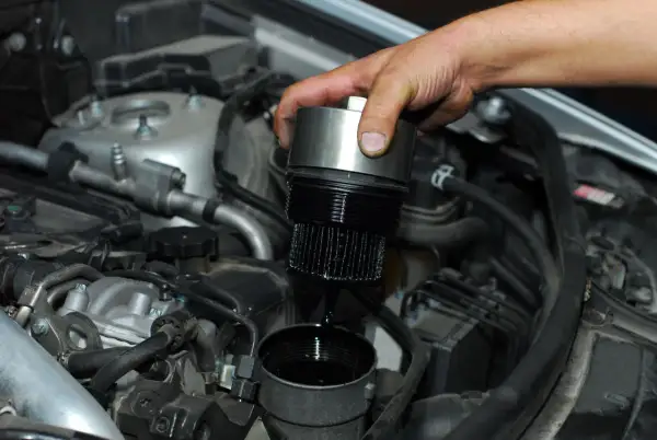 Cambio olio motore: un meccanico rimuove il filtro olio esausto, mostrando dove si trova nel vano motore.