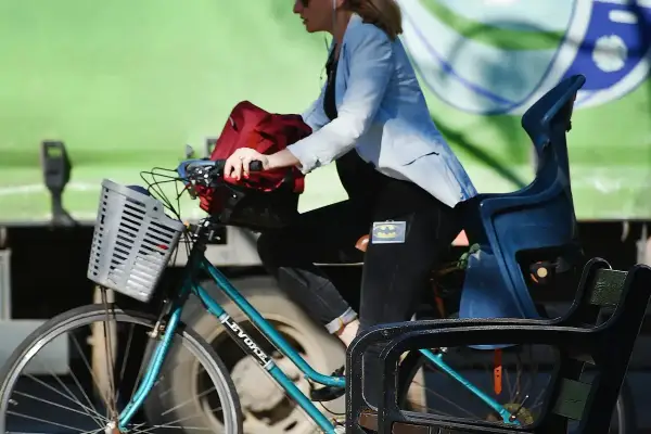 Kobieta w jasnej marynarce i czarnych spodniach z naszywką Batmana jedzie na rowerze. Velo Poprad to jej środek transportu.