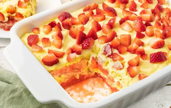 Tiramisù fragole in una teglia bianca, con strati di crema, biscotti e tante fragole fresche a pezzi.