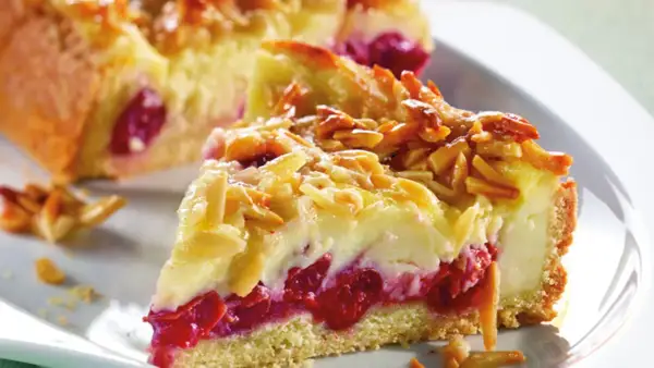 Ein Stück von Omas Kirschkuchen mit Pudding, belegt mit Mandelblättchen. Saftige Kirschen und cremiger Pudding unter knuspriger Kruste.