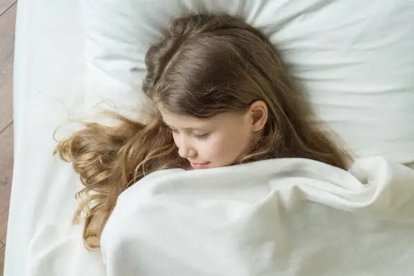 Niña rubia duerme acurrucada, quizás soñando con terrores nocturnos. Su cabello se esparce sobre la almohada blanca.