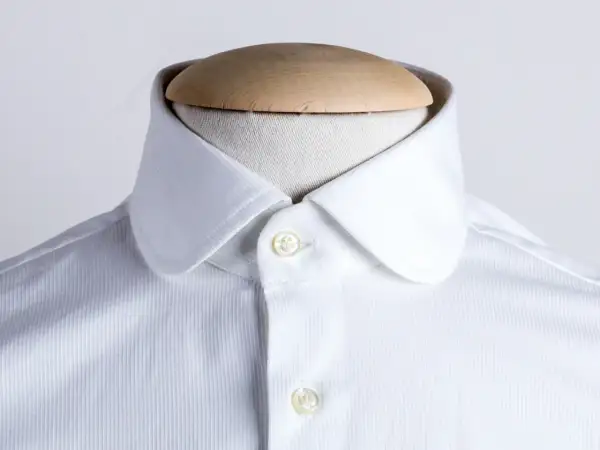 Dettaglio di una camicia bianca con colletto arrotondato, uno dei tanti tipi di colletto camicia, su un manichino.