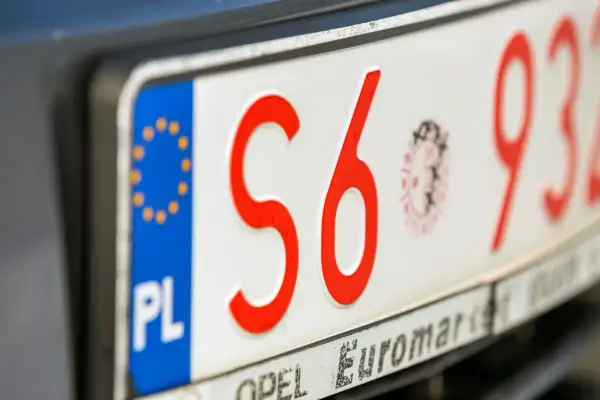 Zbliżenie na polskie tablice rejestracyjne z czerwonymi znakami. Widoczne litery "S6" i cyfry "932".