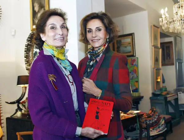 Naty Abascal y otra mujer posan con un libro rojo titulado "100% NATY".