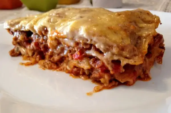 Kawałek zapieczonej lasagne z ciągnącym się serem na białym talerzu.