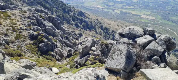 Rocas y vegetación en el cancho del águila, con un valle verde y camino serpenteante al fondo.