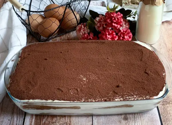 Tiramisù pronto per essere gustato! La ricetta tiramisù con 500 g mascarpone è un classico. Uova, fiori e latte completano la scena.