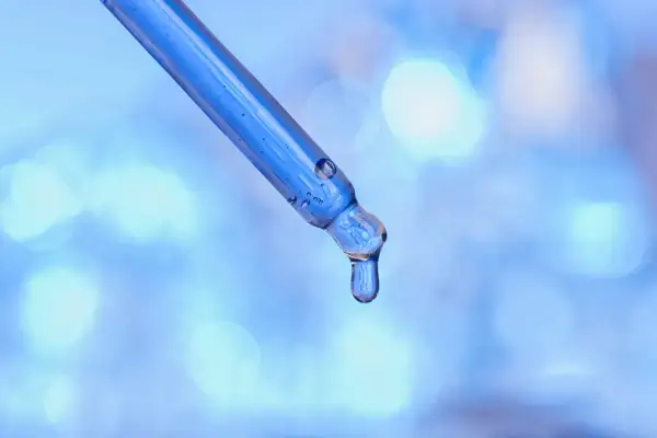 Kropla błękitnego serum, zawierającego peptyd miedziowy, spływa z pipety na rozmyte, błękitne tło.