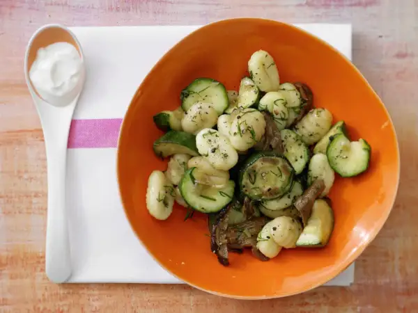Gnocchi mit Zucchini und Pilzen in einer orangen Schüssel, dazu ein Löffel cremiger Dip. Eine köstliche zucchini pfanne.