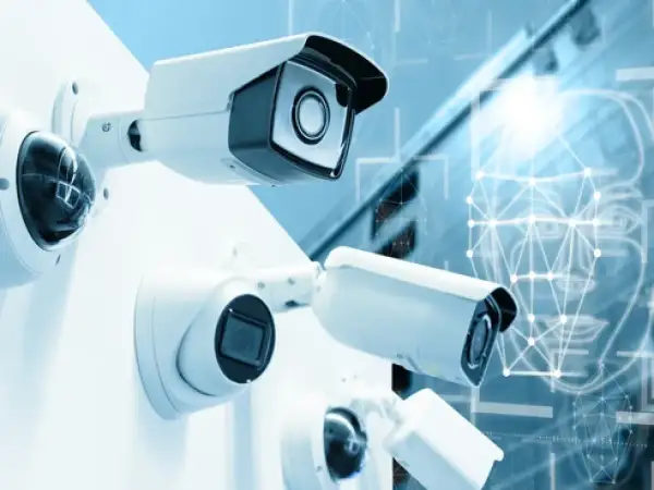 Plusieurs caméras de surveillance sont montées sur un mur blanc. En arrière-plan, un visage stylisé avec des points connectés suggère la technologie de caméra ai.