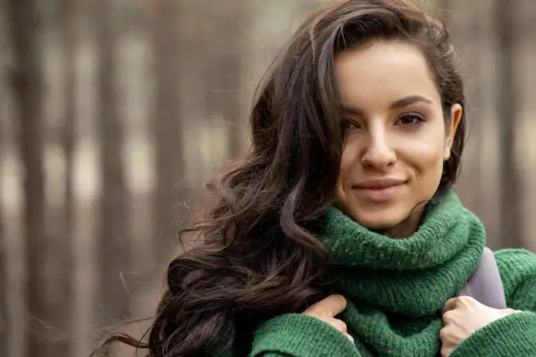 Brunetka w zielonym swetrze, idealne kolory dla brunetek. Jej ciemne włosy falują na wietrze, a uśmiech rozjaśnia twarz.
