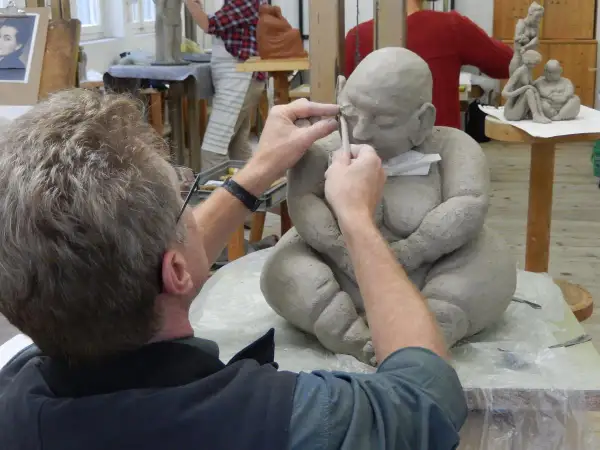 Ein Künstler formt mit Werkzeug eine Tonfigur in einem Atelier.