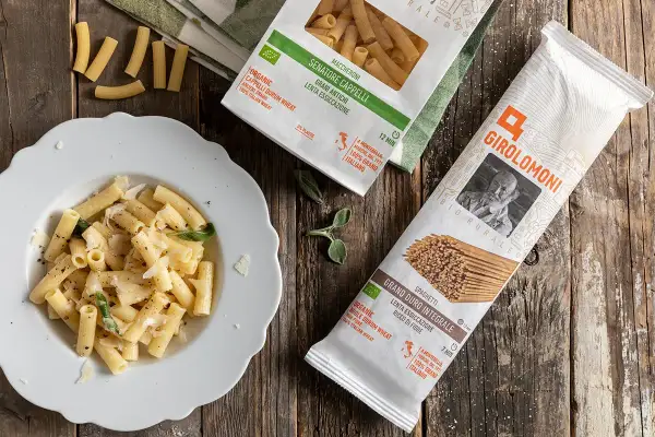 Piatto di maccheroni conditi e pacchi di pasta della Gino Girolomoni Cooperativa Agricola, con grano italiano.