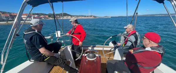 Uomini imparano a navigare durante un corso skipper, con un istruttore che guida il timone.