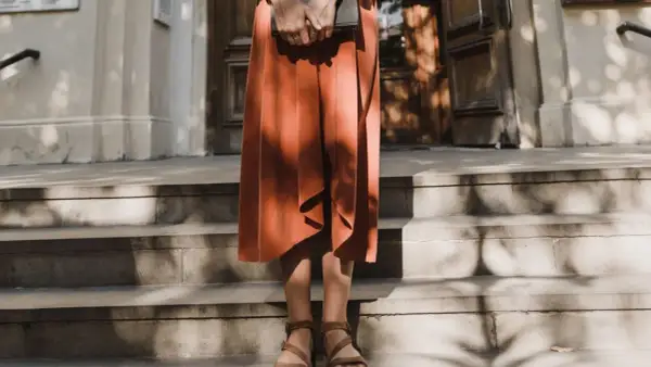 Kobieta w pomarańczowej sukience i sandałach trzyma książkę. Stylizacja idealna do letniego lookbooka.