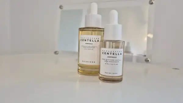 Dwie buteleczki z pipetką zawierające **centella ampoule** od SKIN1004, jedna większa, druga mniejsza, stoją na białej powierzchni.
