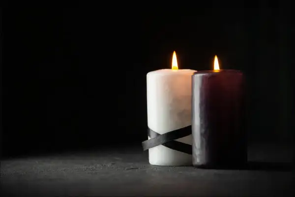 Dwie płonące świece, biała z czarną wstążką i ciemna, symbolizują patologiczną żałobę, która nie ustępuje.