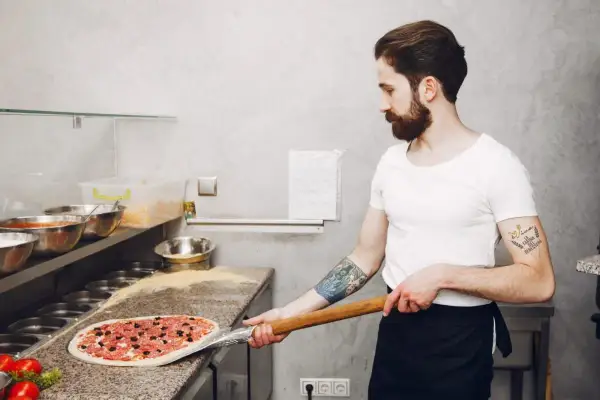 Pizzaiolo con barba prepara una pizza con farina per pizza 0 o 00.