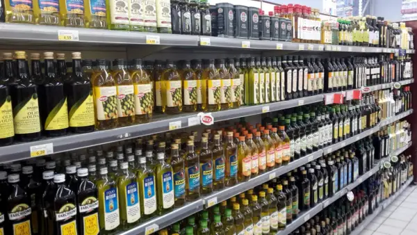 Scaffali di un supermercato pieni di bottiglie di olio d'oliva. Quante olive per un litro di olio? La risposta è nella varietà di marche e formati.