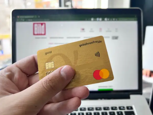 Goldene Kreditkarte mit "gebührenfrei.de" und Mastercard-Logo vor einem Laptop mit BILD-Logo. Erste Erfahrungen mit der Advanzia Bank.
