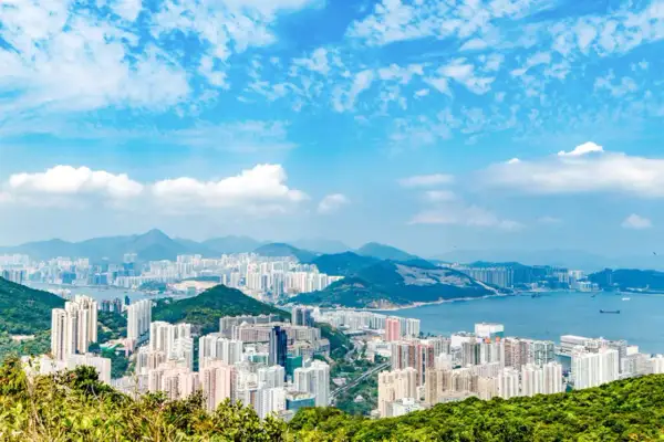 Vy över Hong Kongs tätbefolkade kustlinje med berg i bakgrunden och en blå himmel med moln.