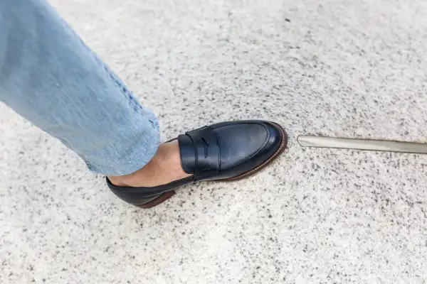 Un homme en jean bleu porte une chaussure de ville marine. L'outil à côté suggère une envie de ressemeler chaussures.