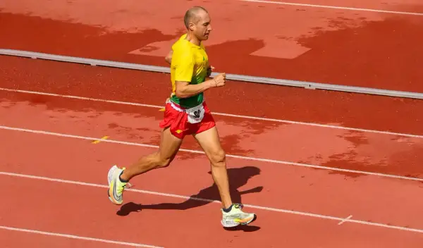 Un athlète en tenue jaune et rouge court sur une piste mouillée, visant le record du monde de vitesse à pied.