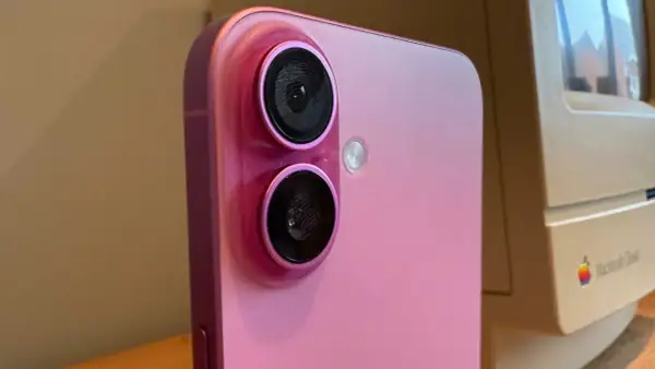 Rosa iPhone med dubbla linser på kameran, bredvid en gammal Macintosh-dator.