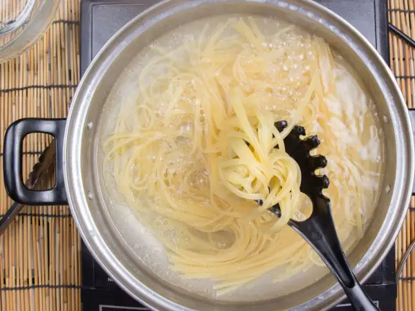 Spaghetti kochen in sprudelndem Wasser. Ein schwarzer Pastalöffel hebt eine Portion heraus, um zu zeigen, wie kleben spaghetti nach dem kochen nicht zusammen.