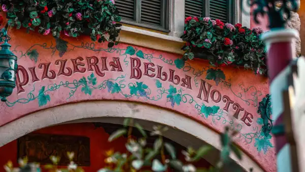 Różowa fasada Pizzerii Bella Notte ozdobiona winoroślą i kwiatami.