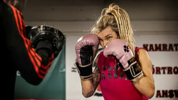 Mikaela boxare i rosa handskar, redo för träning. Hennes blick är fokuserad, med dreadlocks som ramar in ansiktet.